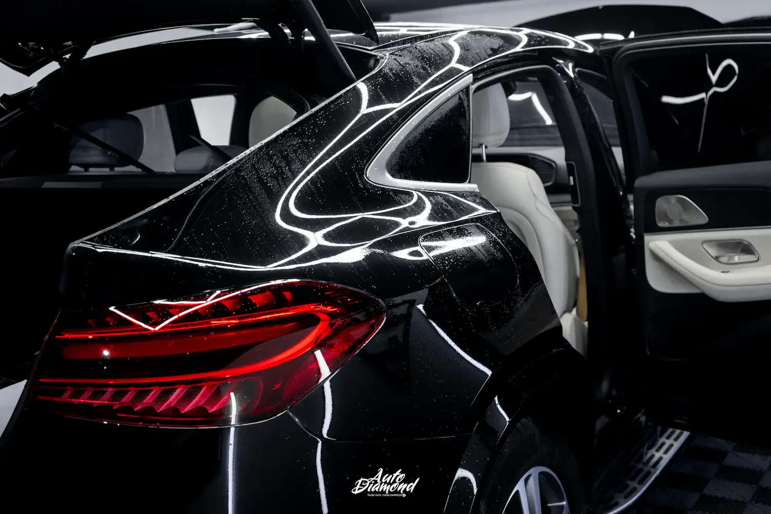 Technik Auto Diamond nakłada folię PPF rękami na maskę czarnego samochodu